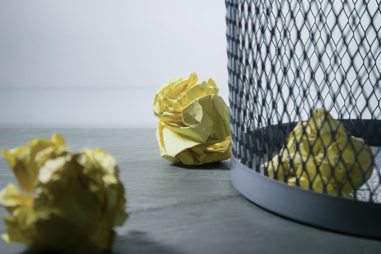 Services Close-up of crumpled yellow paper around a mesh trash bin, symbolizing rejected ideas or recycling.
